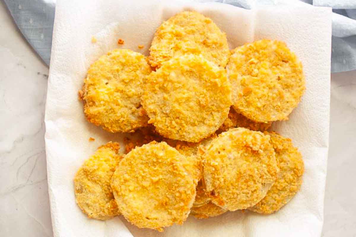 A plate of golden-brown fried green tomato slices on a paper towel, seen from above.