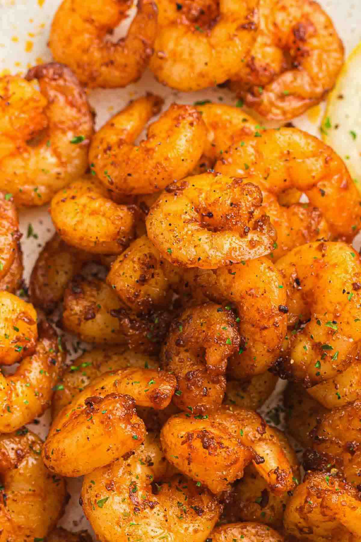 Close-up of cooked shrimp coated in reddish-brown seasoning, garnished with finely chopped herbs.