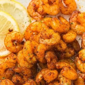 Close-up of seasoned, cooked shrimp garnished with herbs, with lemon slices on the side.