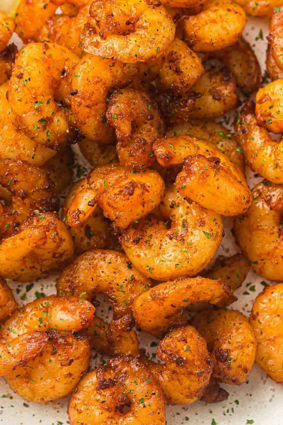 Close-up of cooked shrimp seasoned with spices and garnished with chopped herbs.