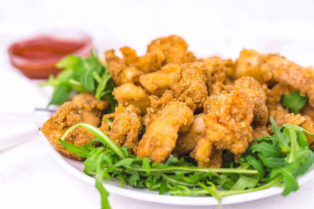 A plate of fried chicken pieces served on a bed of fresh arugula, with a small bowl of dipping sauce in the background.