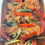 Baked chicken breasts with sliced red and green bell peppers and onions in a dark seasoned sauce.