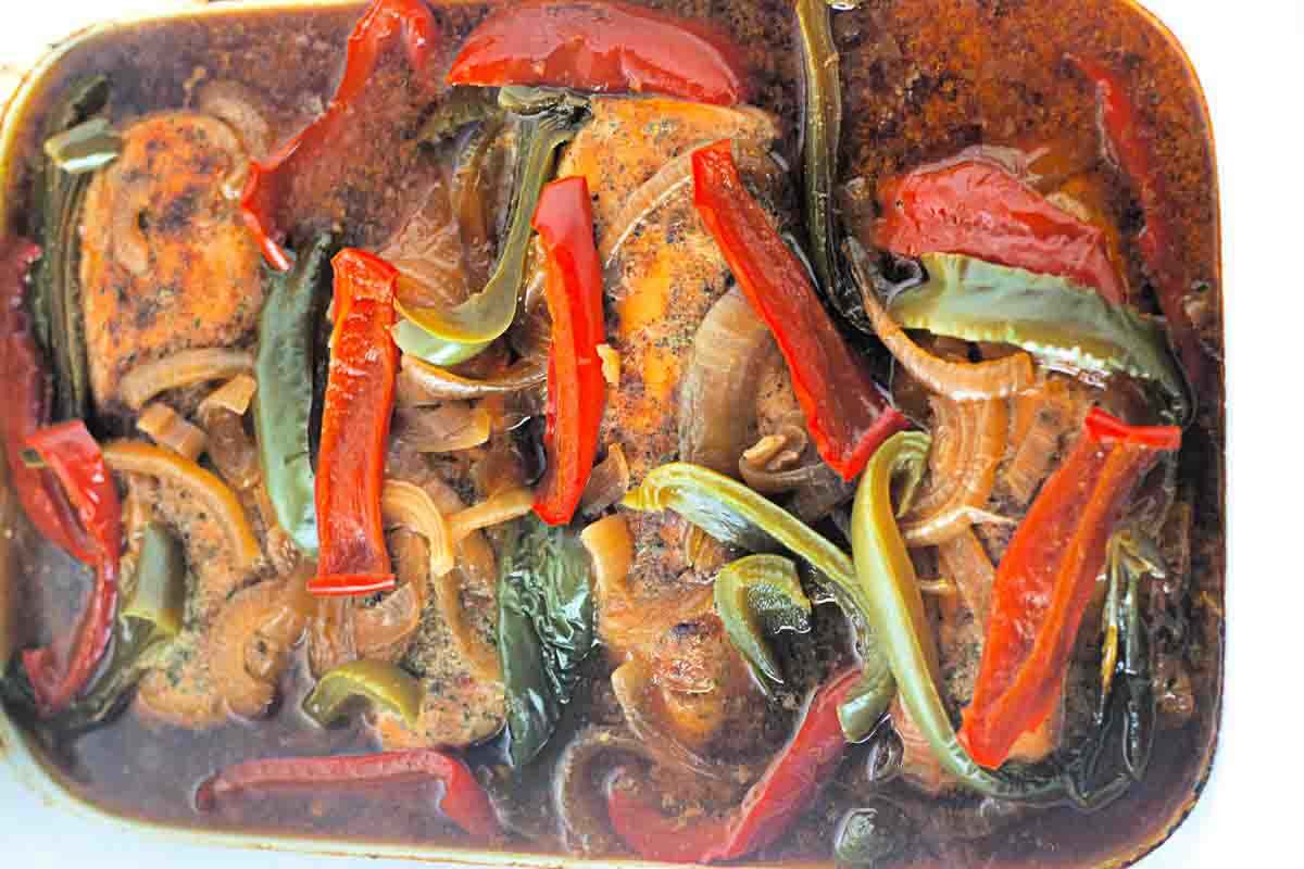 Slow cooked chicken breasts in a brown sauce, topped with sliced red and green bell peppers and onions.