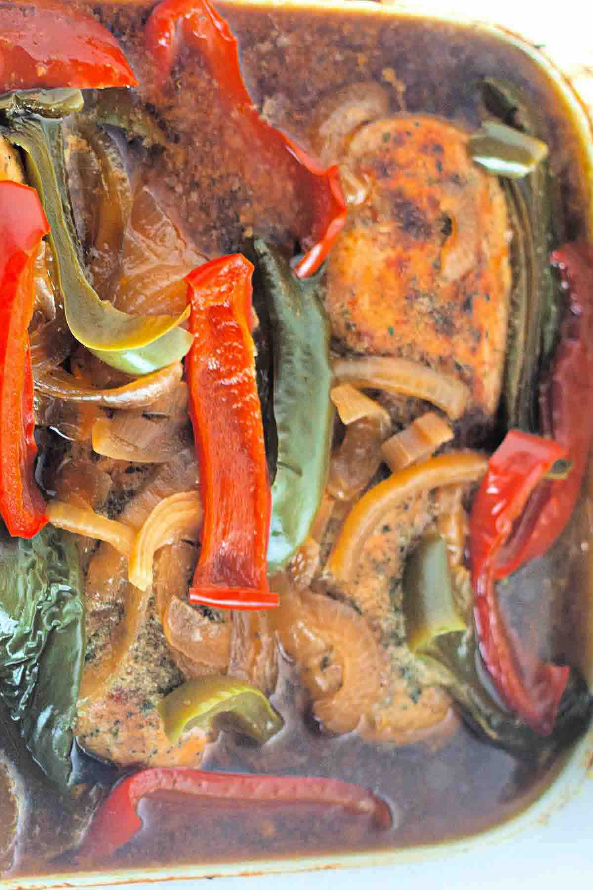 Baked chicken breast with sliced red and green bell peppers, onions, and a dark sauce in a casserole dish.