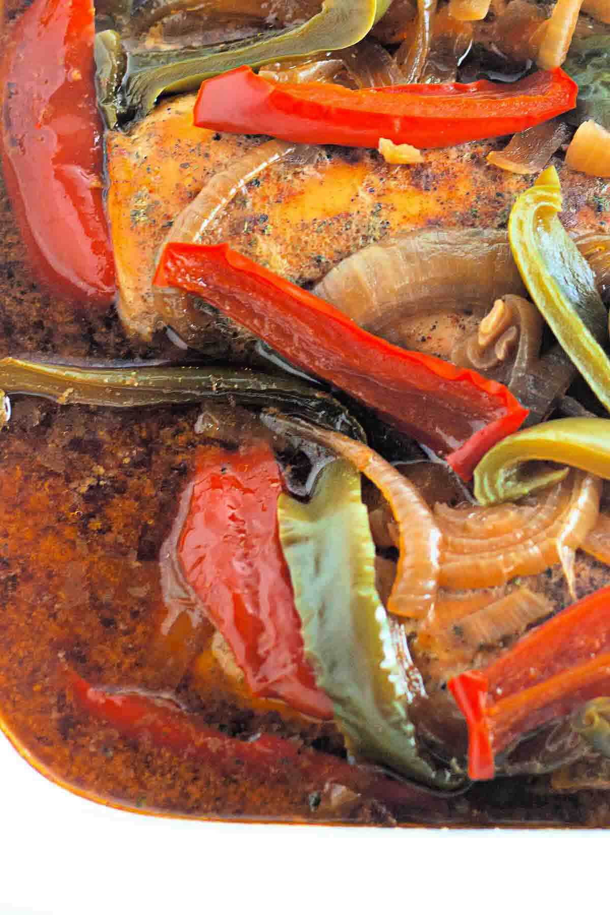 Close-up of baked fish fillet topped with sliced red and green bell peppers and onions in a seasoned sauce.