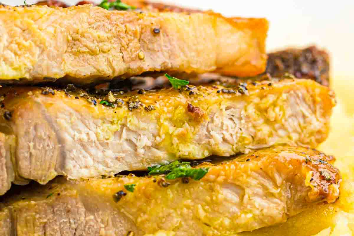 Close-up of three thick, cooked pork chops stacked on top of each other, seasoned with herbs and pepper.