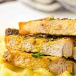 Close-up of sliced, seasoned pork chops stacked on a bed of mashed potatoes, garnished with herbs.