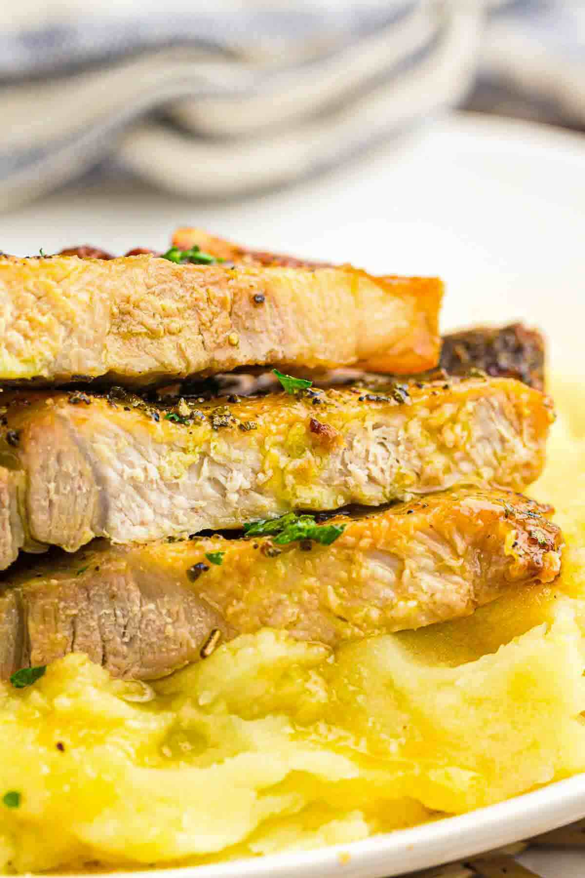 Three thick slices of cooked pork loin are stacked on top of mashed potatoes, garnished with herbs, on a white plate.
