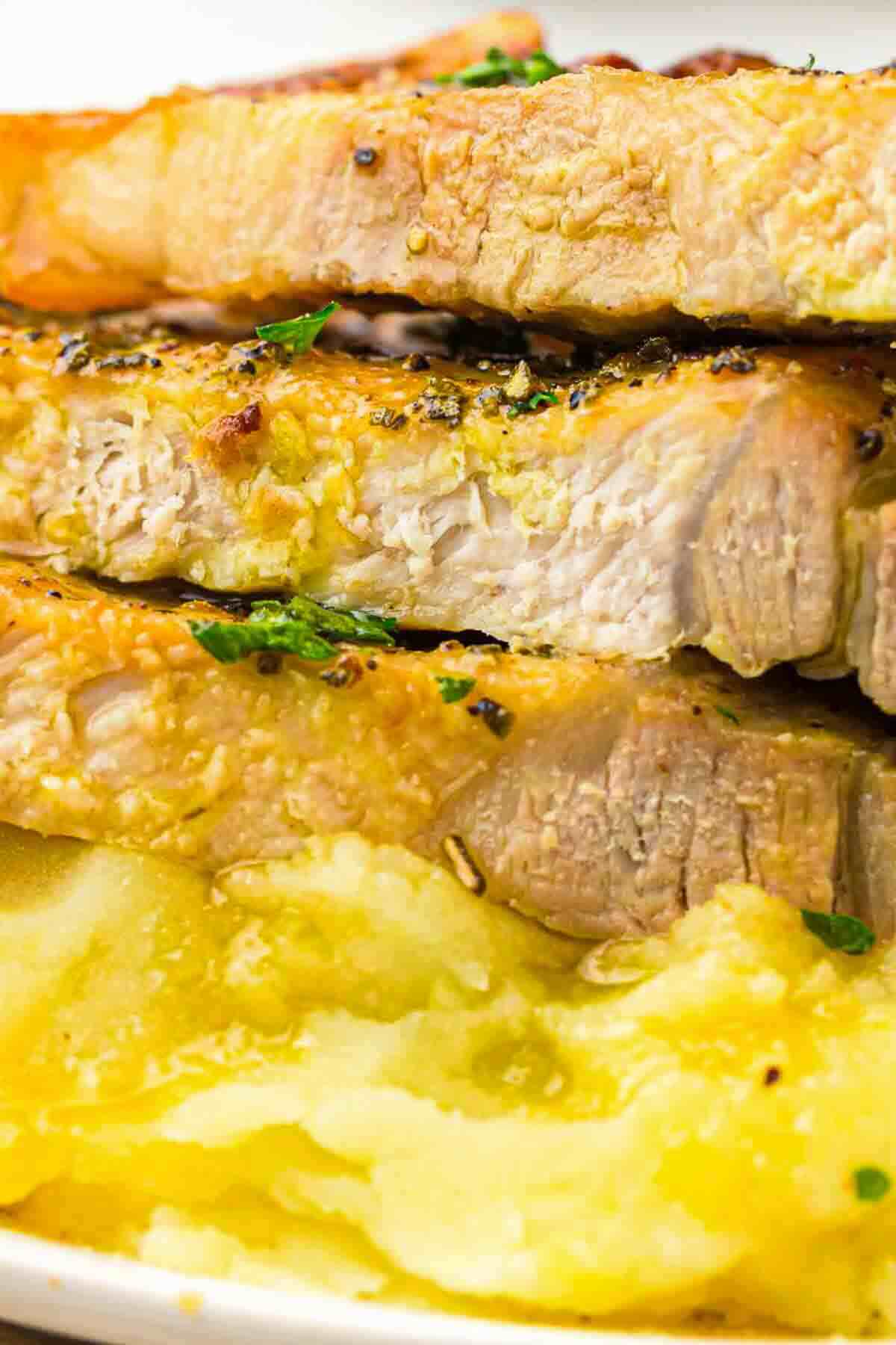 Three slices of cooked pork with a golden crust served on a bed of mashed potatoes, garnished with chopped herbs.
