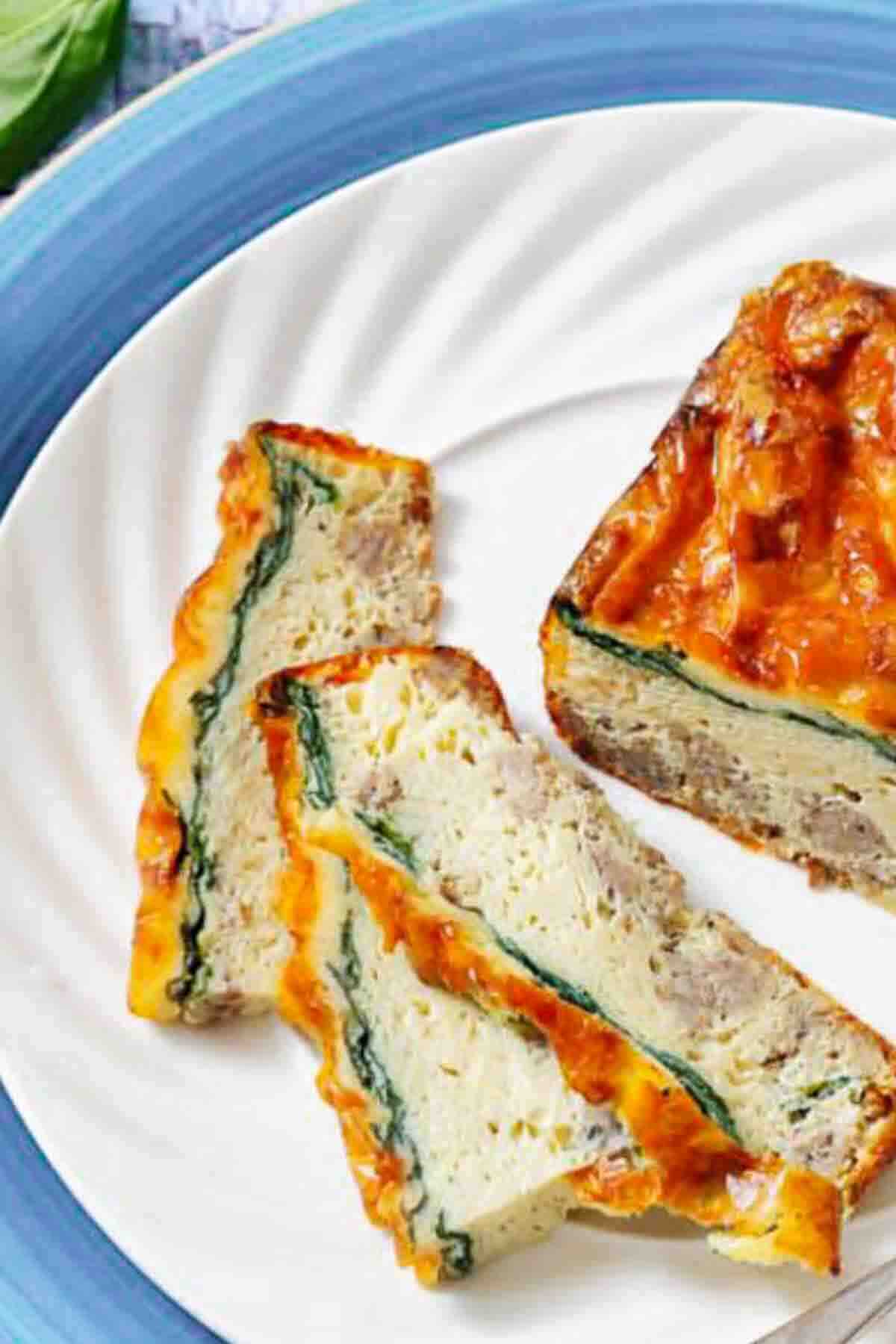 Three slices of a baked egg and spinach casserole are arranged on a white plate with a blue rim.