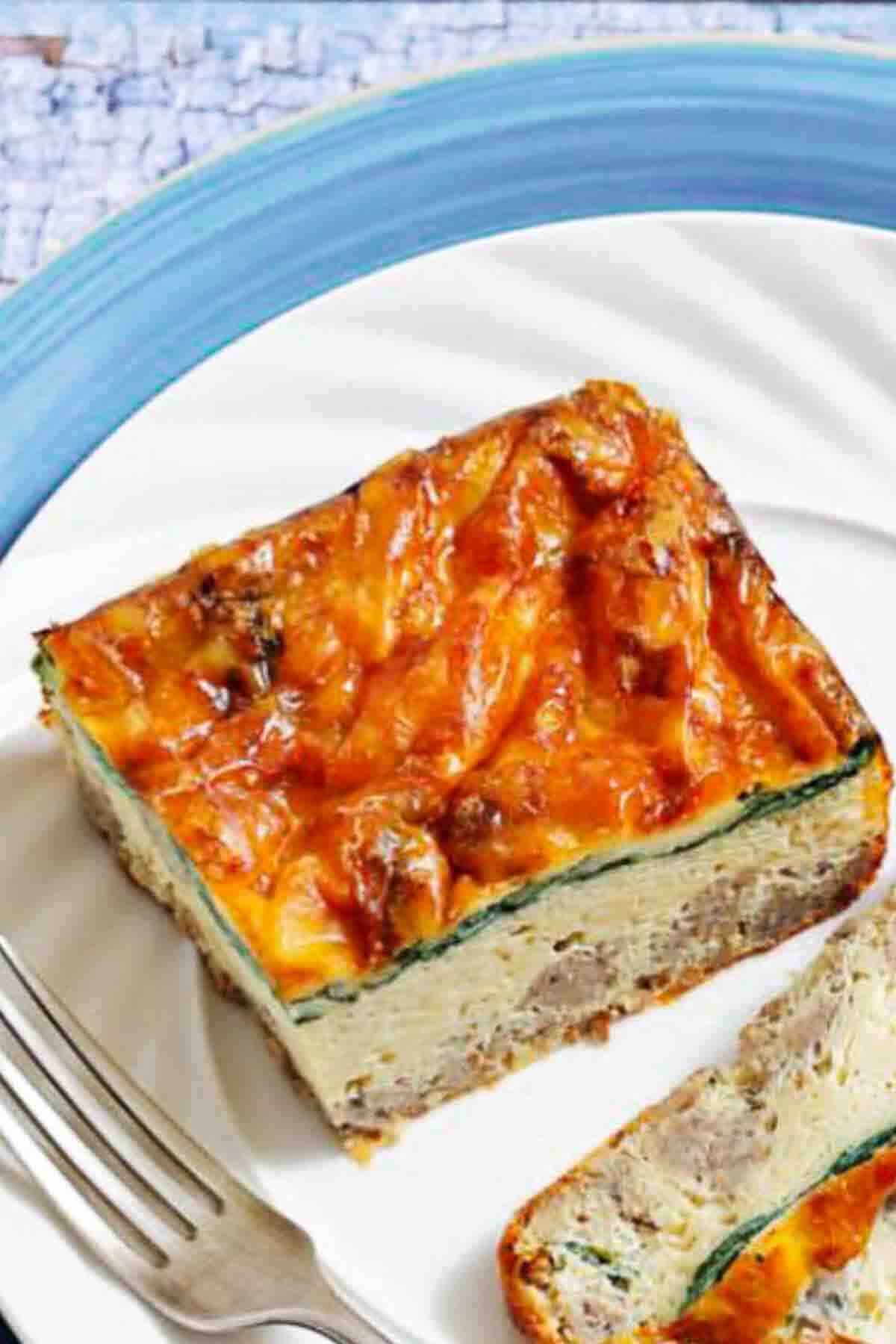 A square slice of baked casserole with a golden-brown cheesy top sits on a white plate next to a fork.