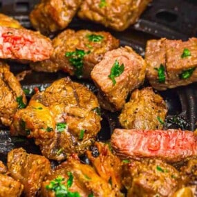 Close-up of cooked steak bites on a grill pan, garnished with chopped parsley. Some pieces show a medium-rare doneness with a pink interior.