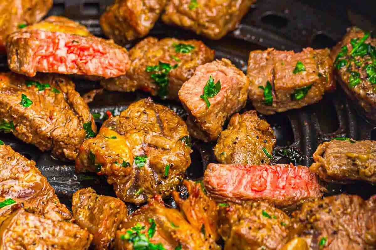 Close-up of cooked steak bites on a grill pan, garnished with chopped parsley. Some pieces show a medium-rare doneness with a pink interior.