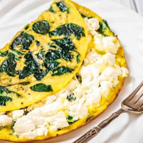 A spinach and feta cheese omelette folded in half on a white plate, with a fork placed beside it.