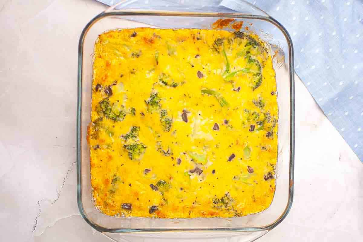 A square glass baking dish filled with a baked casserole containing broccoli and red onions, placed on a light countertop.