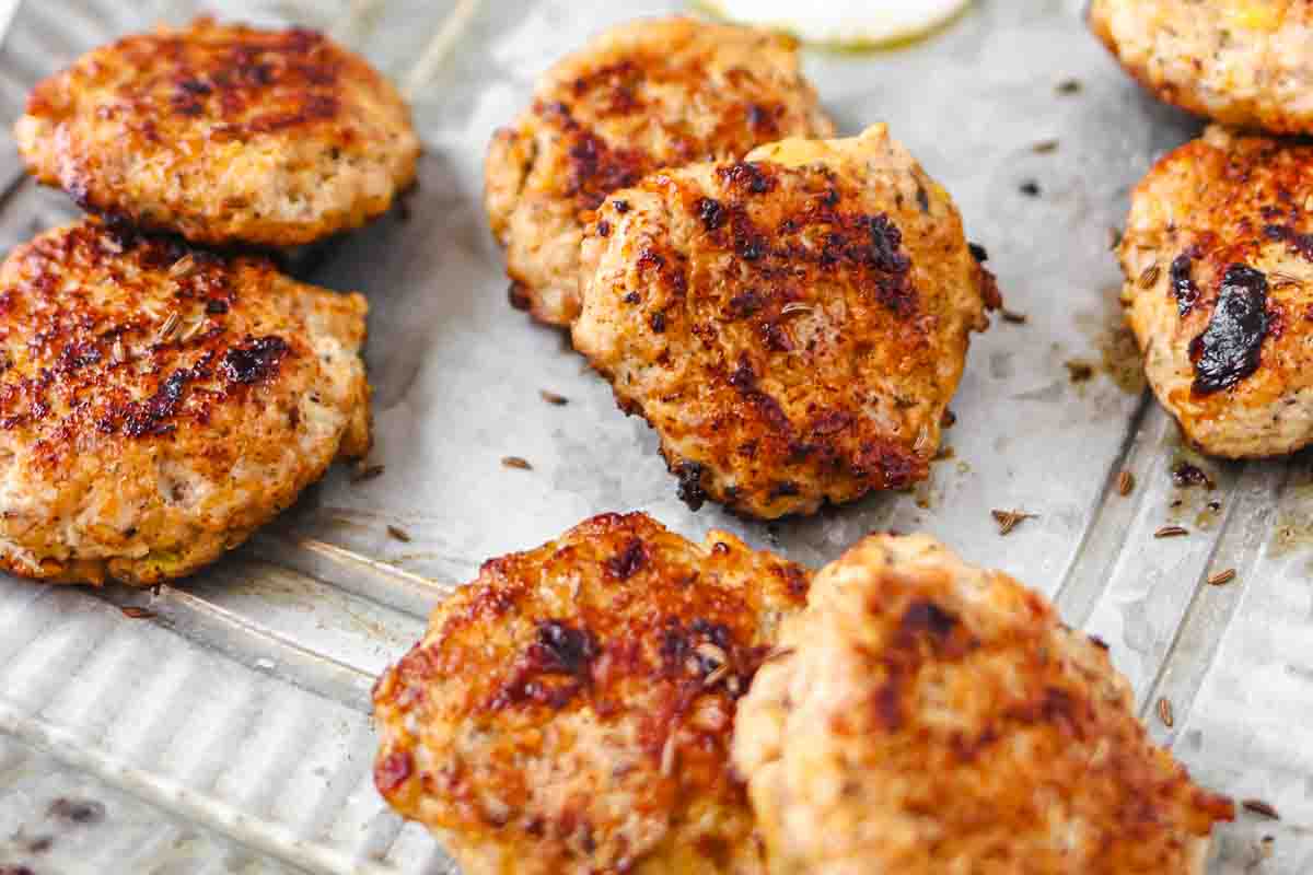 Several browned, round chicken patties are arranged on a baking tray.
