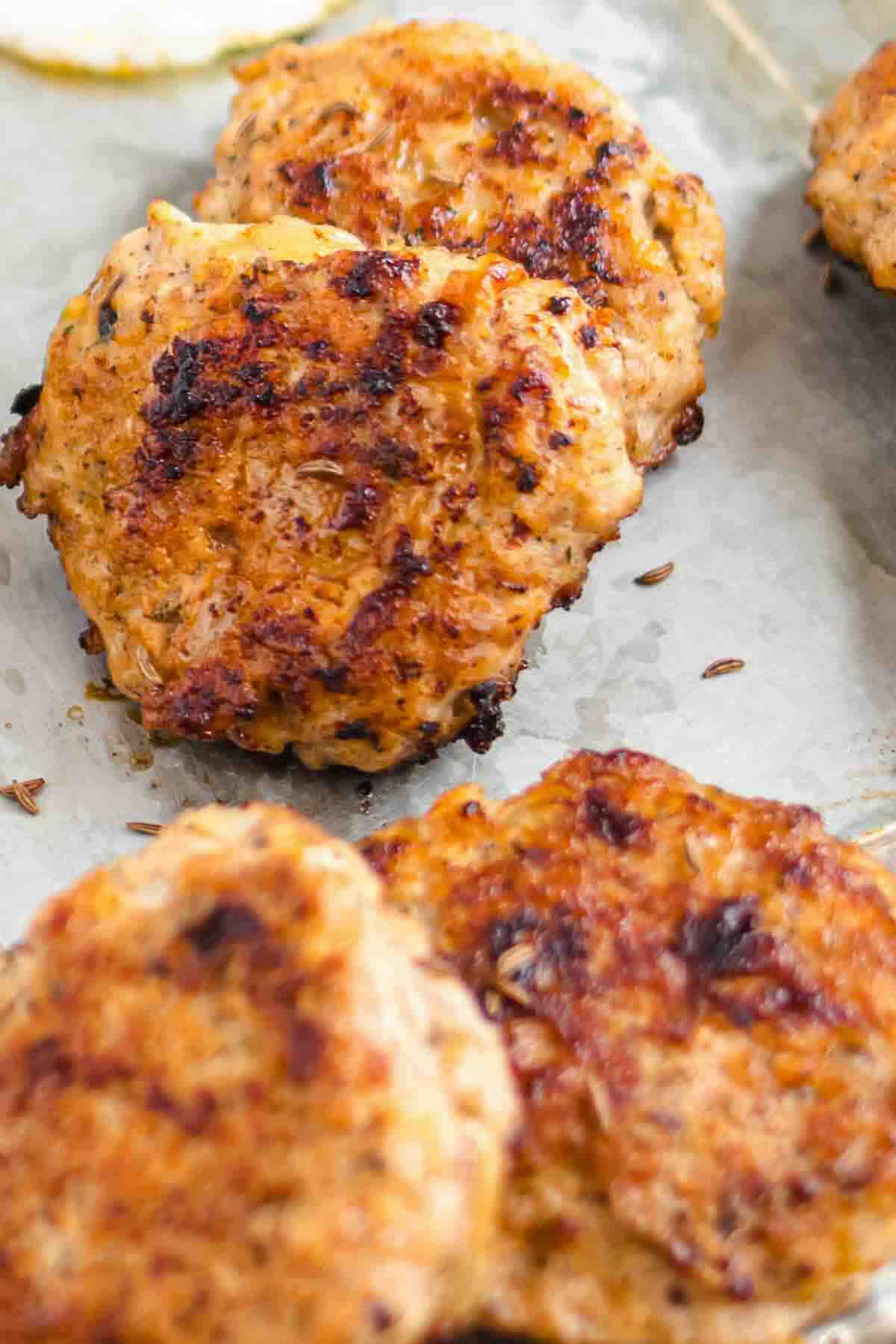 Four browned turkey patties are shown on a parchment-lined baking sheet, displaying a crispy, seared exterior.