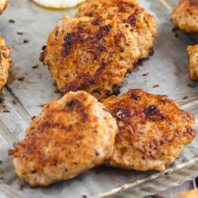 Several browned sausage patties are arranged on a metal tray, showcasing a crispy, cooked exterior.