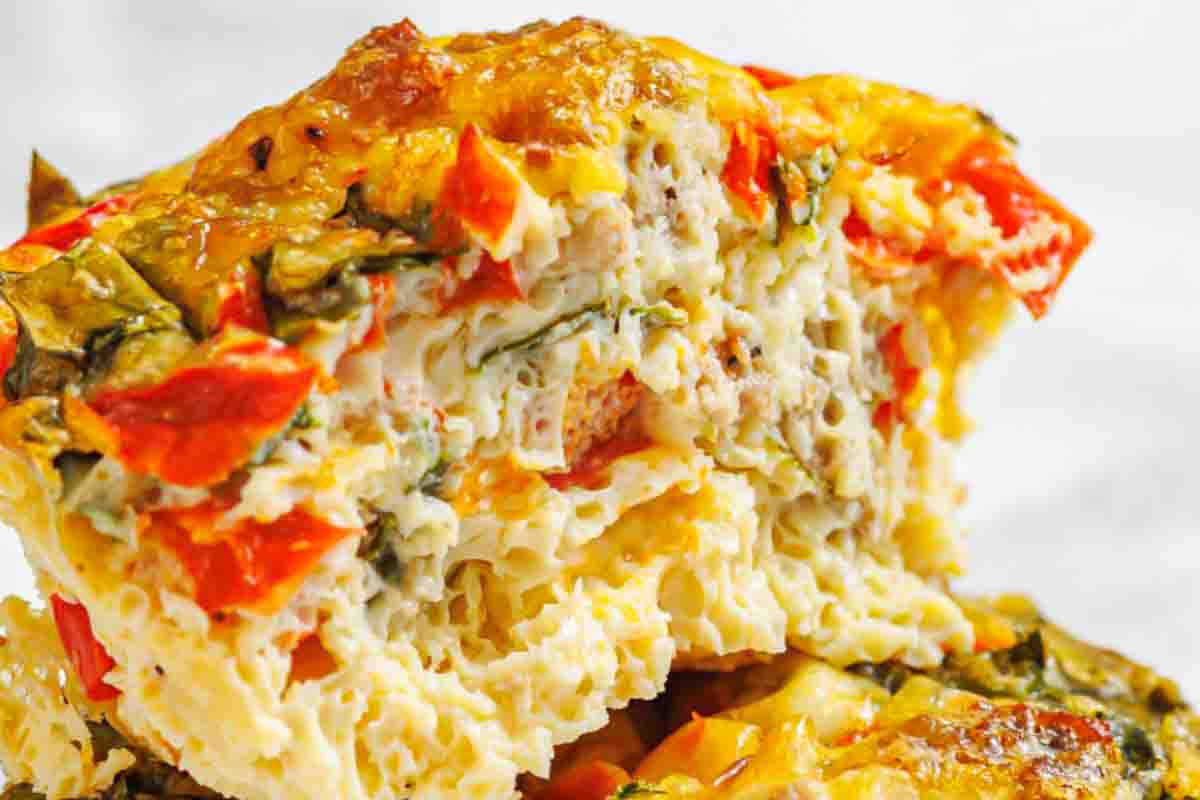 Close-up of a sliced egg muffin with visible chunks of red bell pepper, spinach, and bits of sausage.