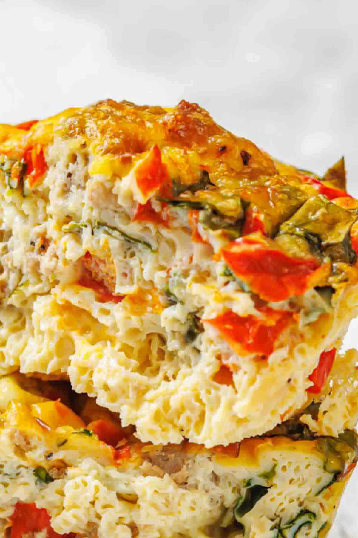 Close-up of a baked egg muffin filled with red bell peppers, spinach, and cheese, showing a moist and fluffy texture.