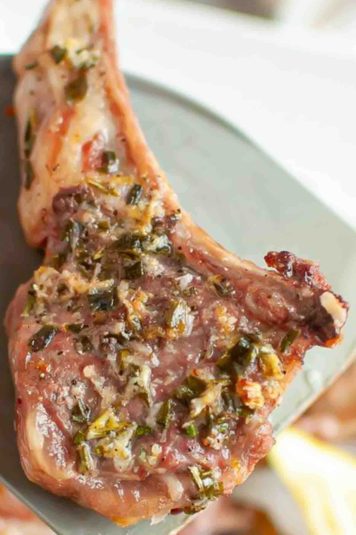 A cooked lamb chop on a plate, seasoned with herbs and garlic.