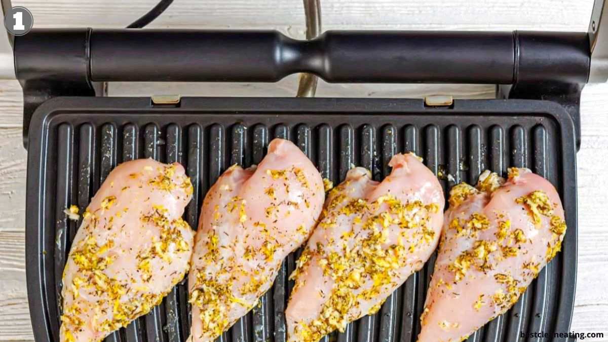 Four raw, seasoned chicken breasts placed side by side on an electric grill, ready to be cooked.