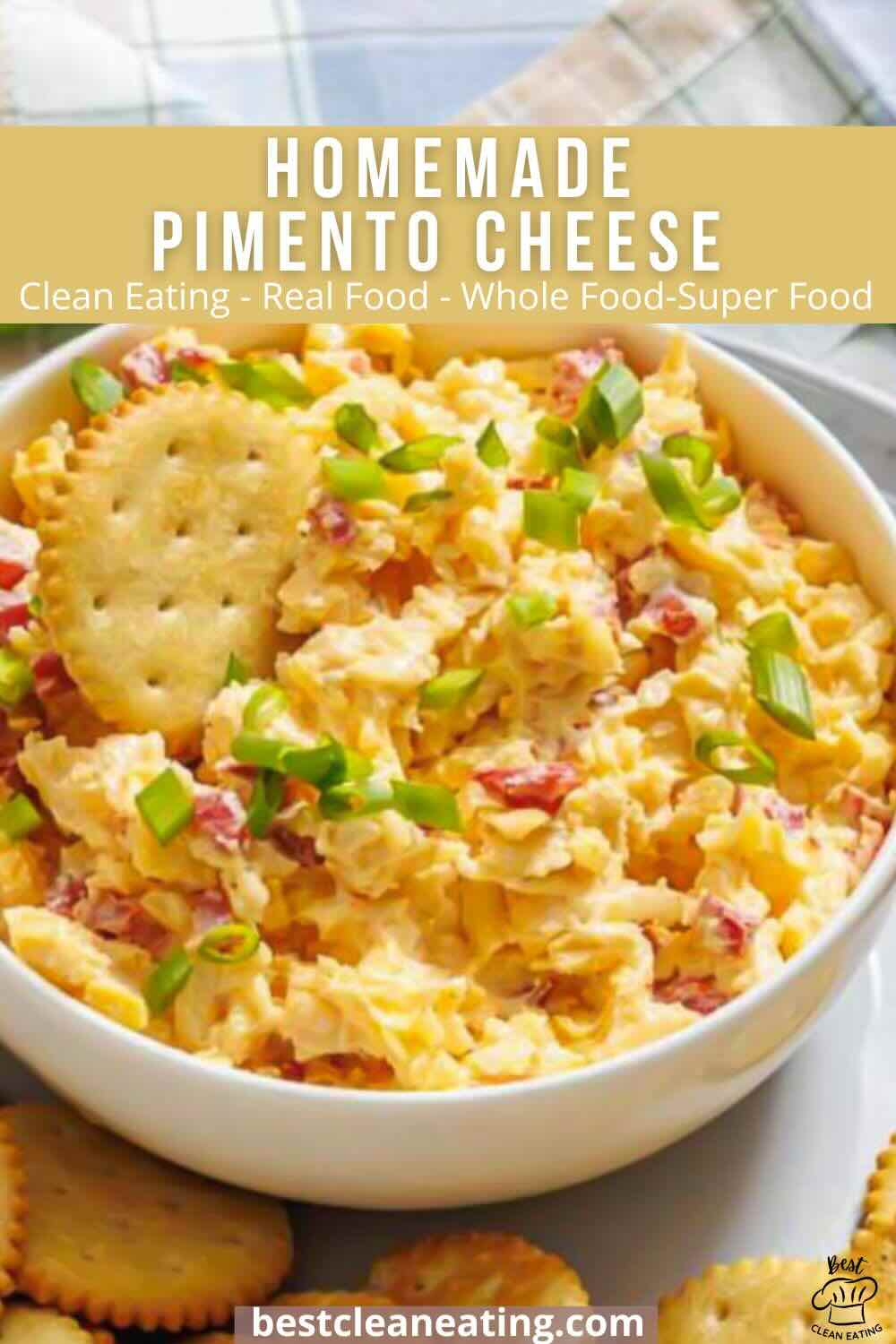 A bowl of homemade pimento cheese garnished with green onions, surrounded by round crackers on a table.