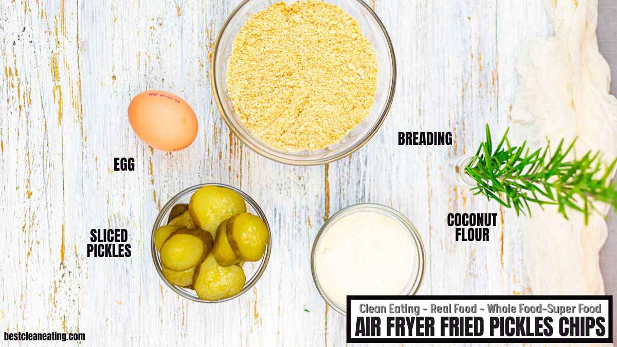 Ingredients for air fryer fried pickle chips: a whole egg, a bowl of breading, a bowl of coconut flour, and a bowl of sliced pickles on a white wooden surface.