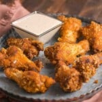 A metal plate with several pieces of crispy fried chicken wings and a square dish of creamy dipping sauce on the side.