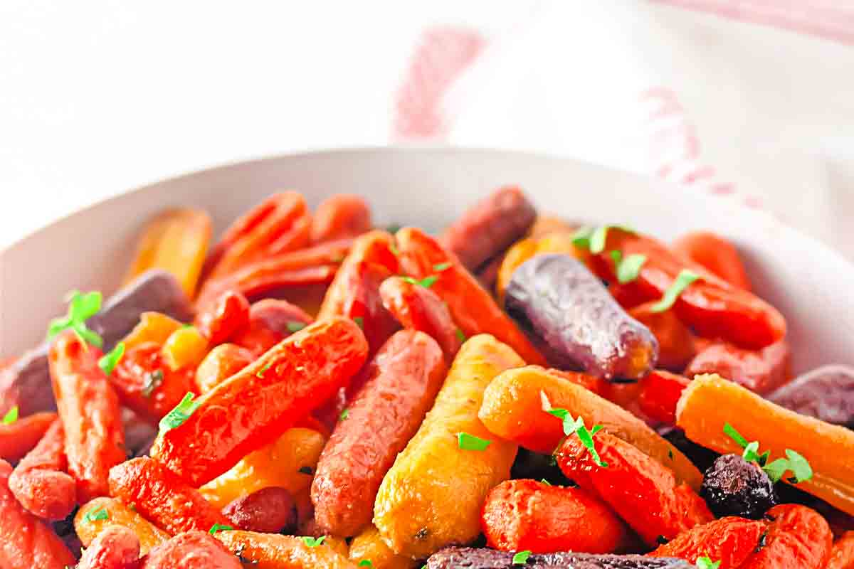 A bowl filled with glazed baby carrots in various colors, garnished with small green herb pieces.