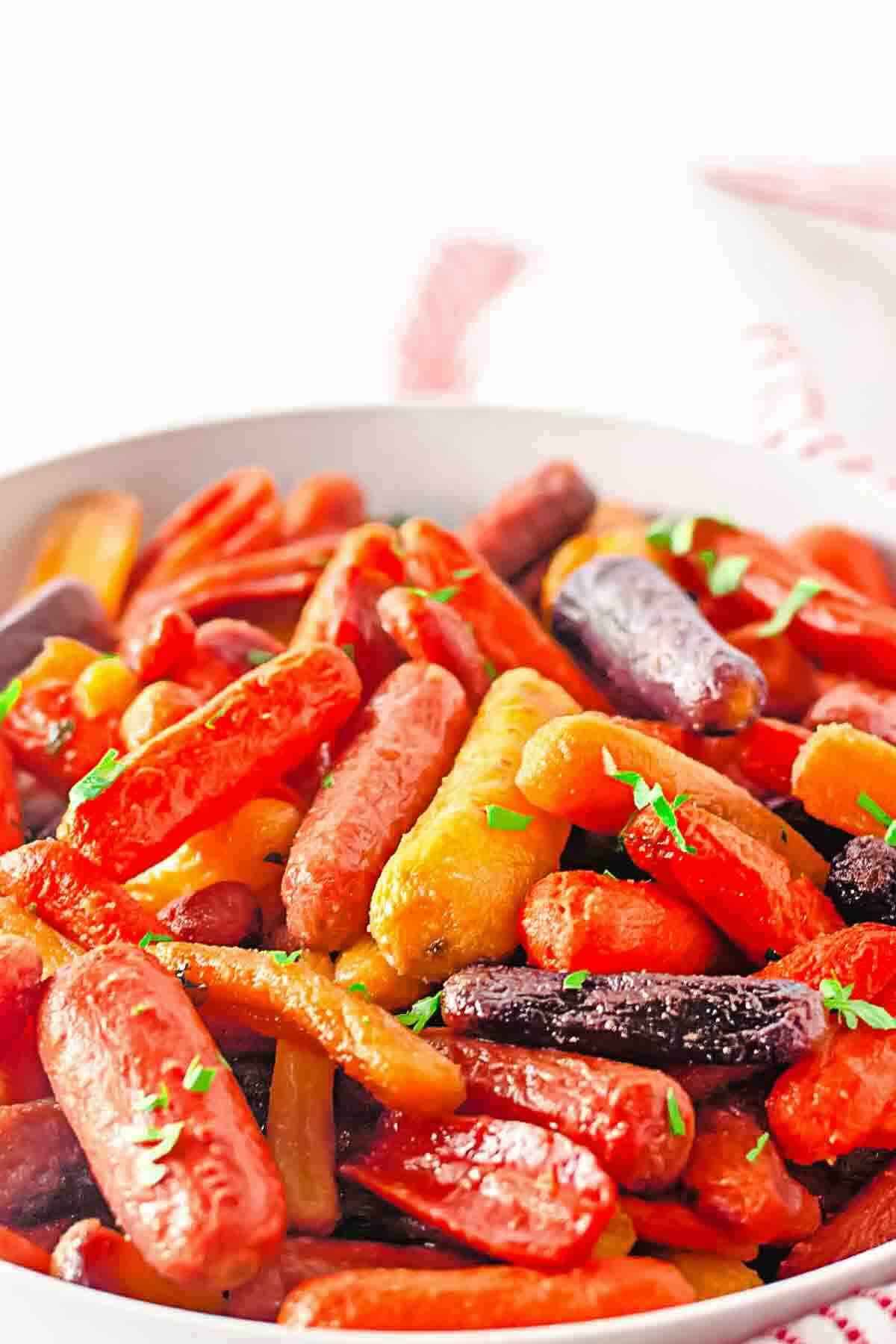 A bowl of roasted multicolored baby carrots garnished with chopped herbs.