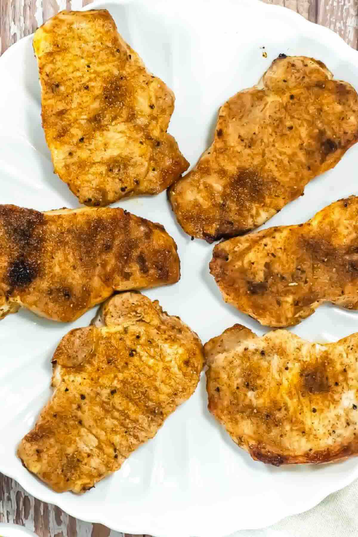 Six cooked, seasoned pork chops arranged in a circular pattern on a white plate.