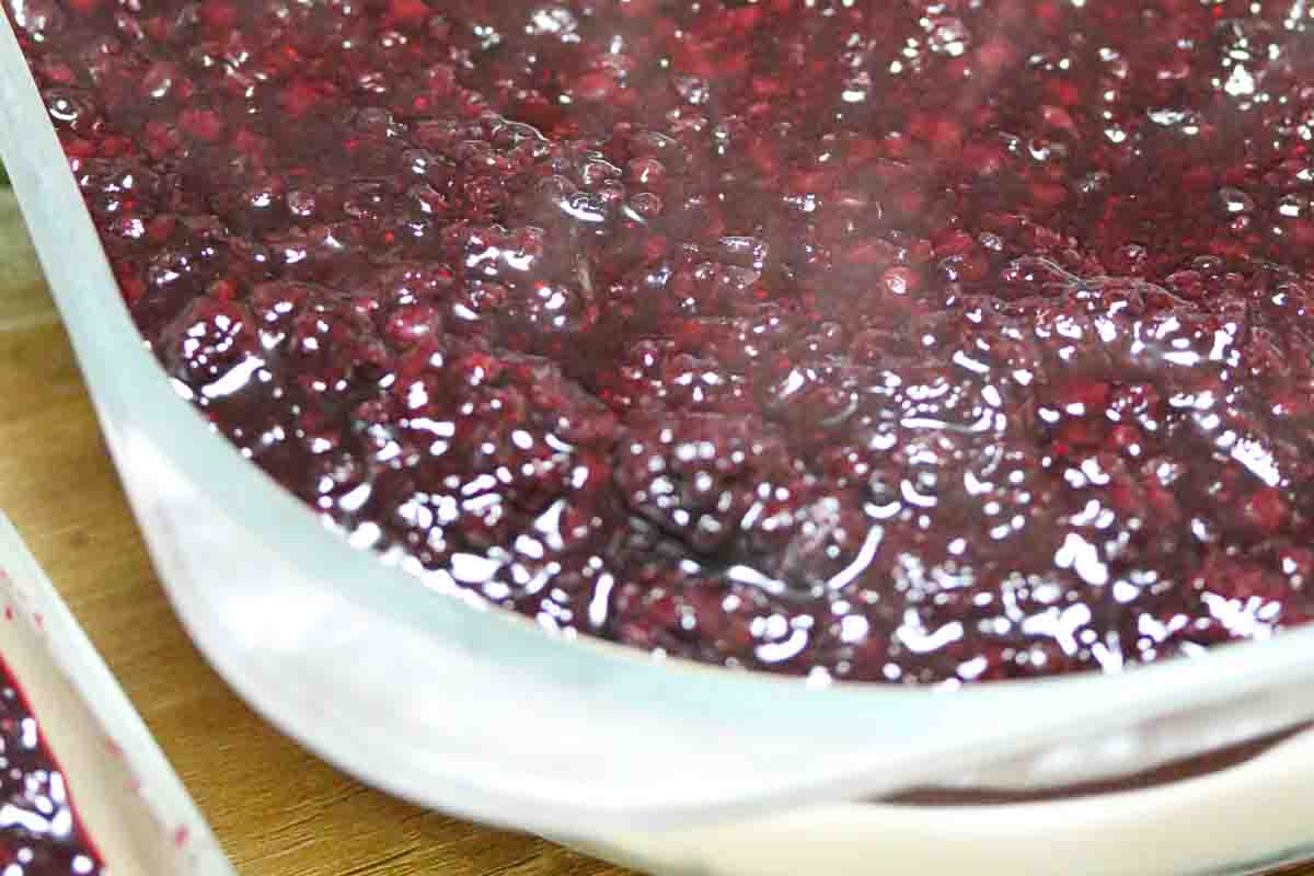 Close-up of a glass dish filled with thick, glossy blackberry compote.