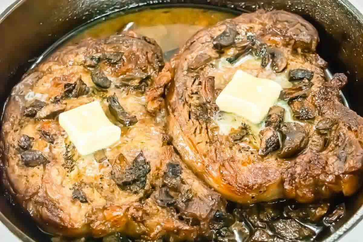 Two roasted prime rib steaks with mushrooms and butter surrounded by pan juices.