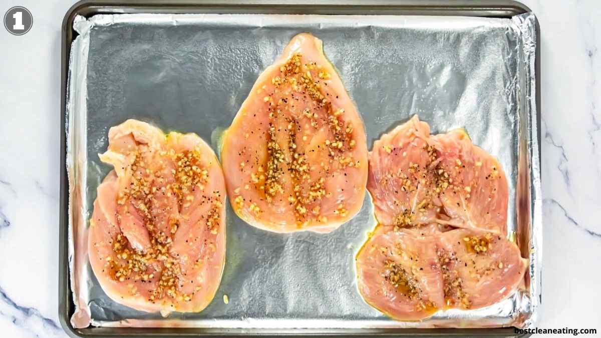 Three raw, seasoned chicken breasts laid flat on a foil-lined baking sheet, ready to be cooked.