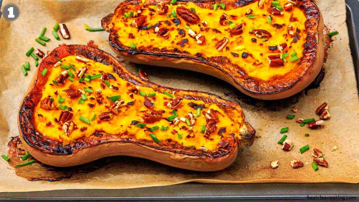 Two baked butternut squash halves with a golden top, garnished with chopped pecans and chives, on a parchment-lined baking tray.