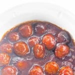 Meatballs coated in a glossy, dark brown sauce inside a white slow cooker.