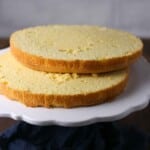 Two round yellow sponge cake layers stacked on a white cake stand, ready for assembling or decorating.