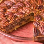 A pecan pie in a glass dish with one slice removed.
