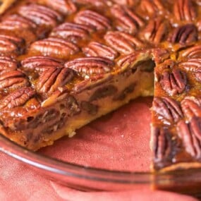 A pecan pie in a glass dish with one slice removed.