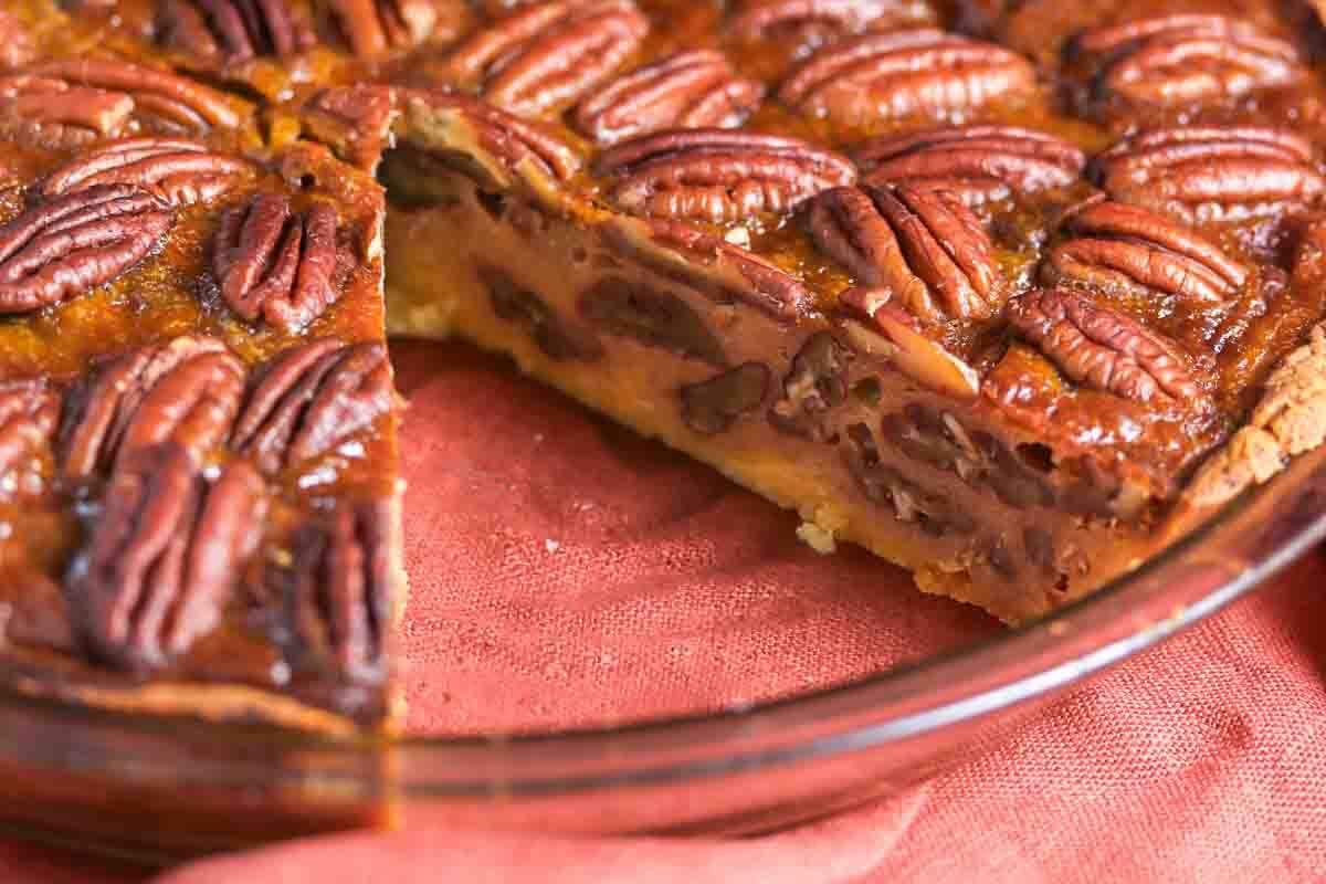 A pecan pie in a glass pie dish with one slice removed.