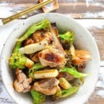A bowl of stir-fried chicken, broccoli, and green onion segments with a pair of chopsticks.