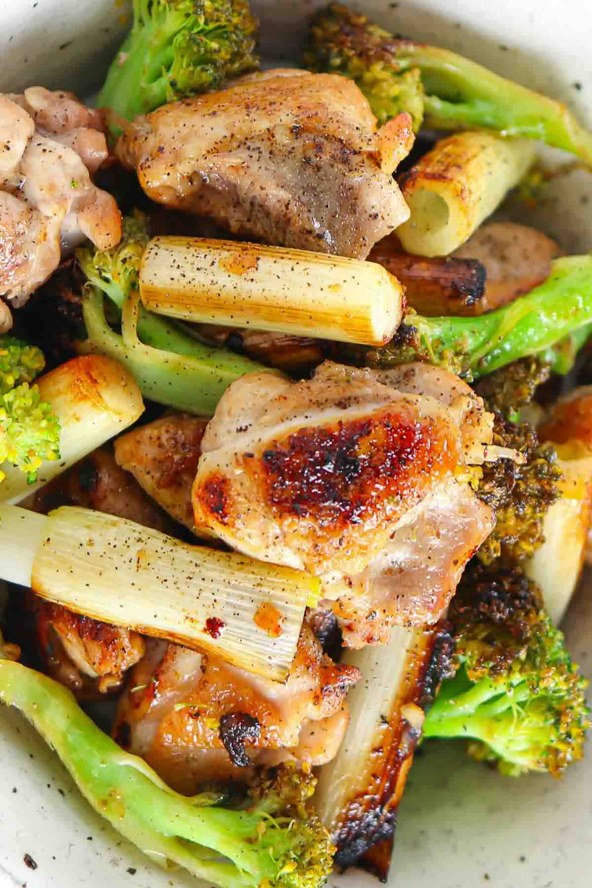 A dish of seared chicken pieces, roasted broccoli, and charred leeks.