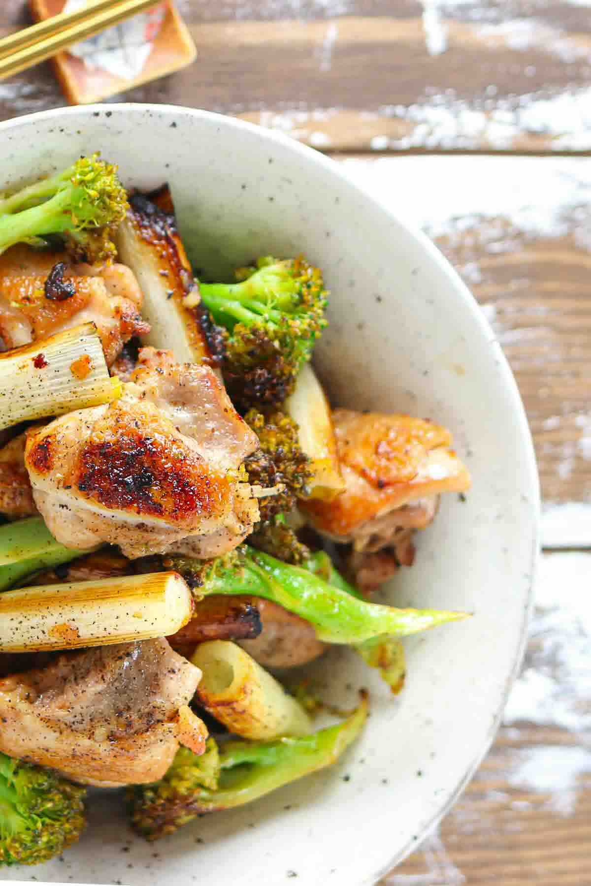 A bowl of stir-fried chicken, broccoli, and scallions.