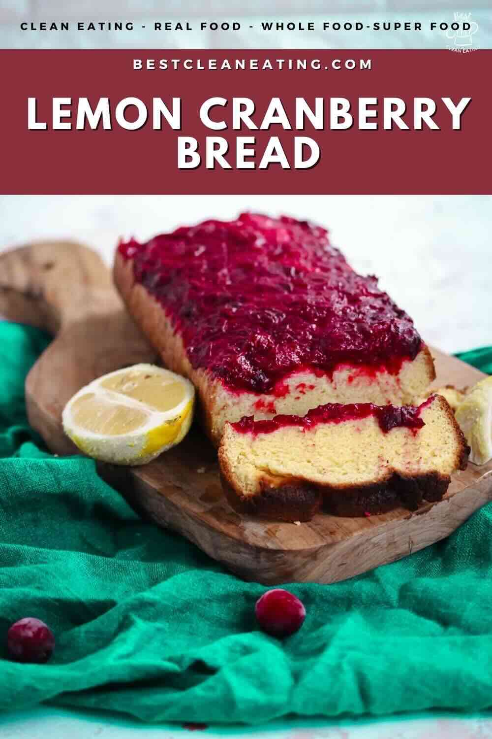 Loaf of lemon cranberry bread topped with cranberry jam on a wooden cutting board with a sliced lemon.